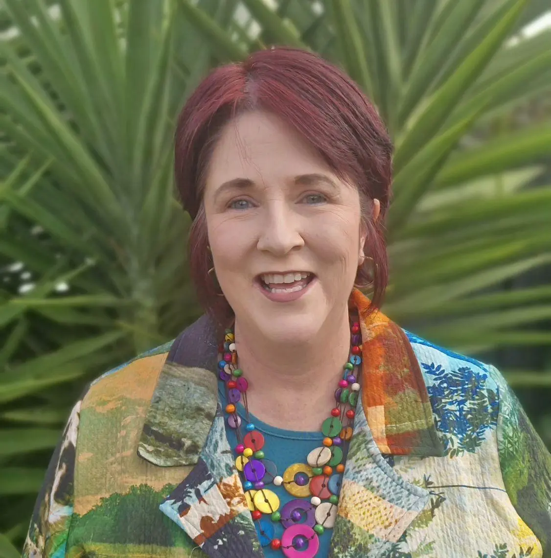 Smiling woman with red hair and colorful necklace outdoors.